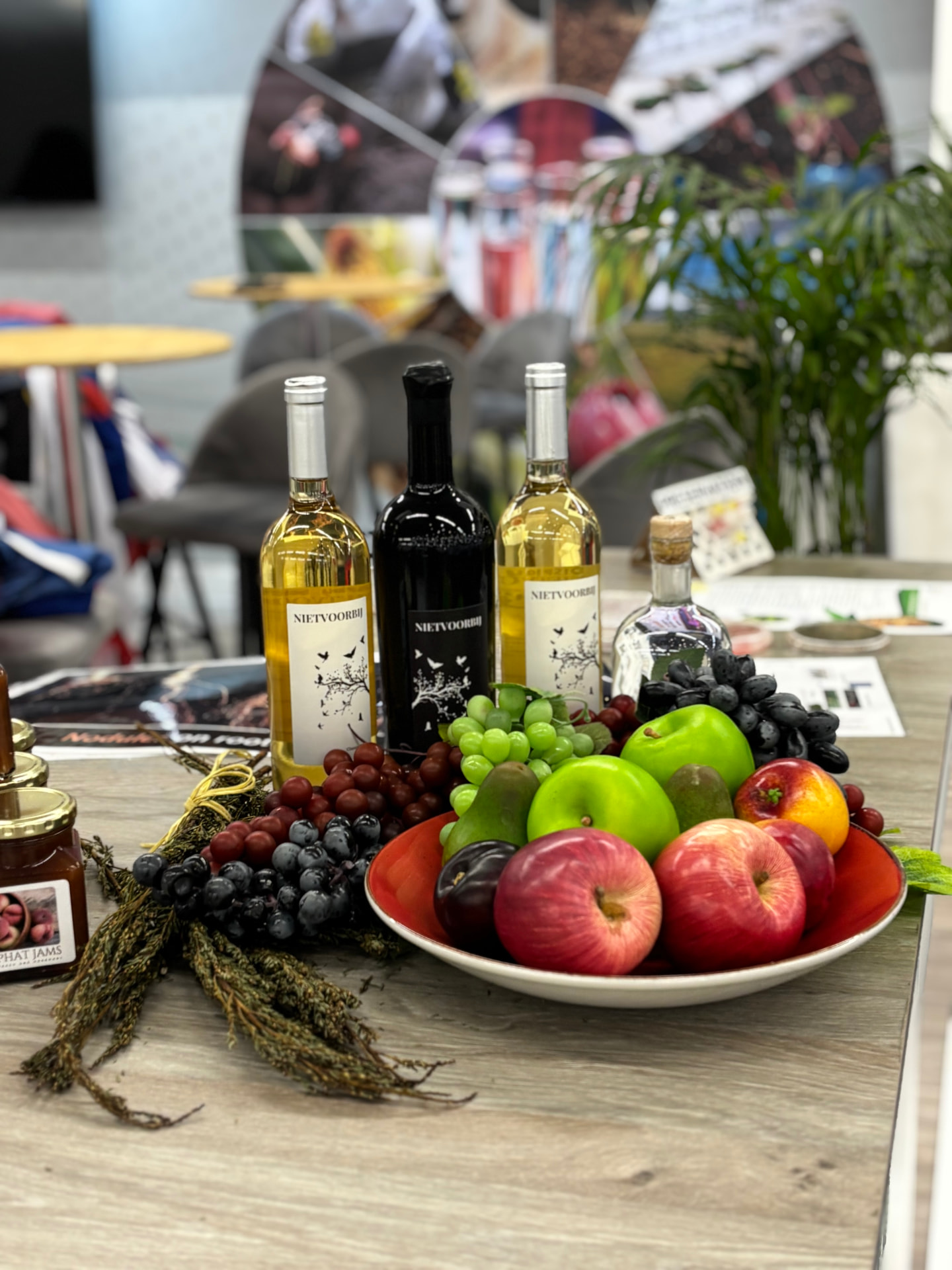 ARC exhibition display with Nietvoorbij wine bottles, preserves and a bowl of fresh fruit on a table.